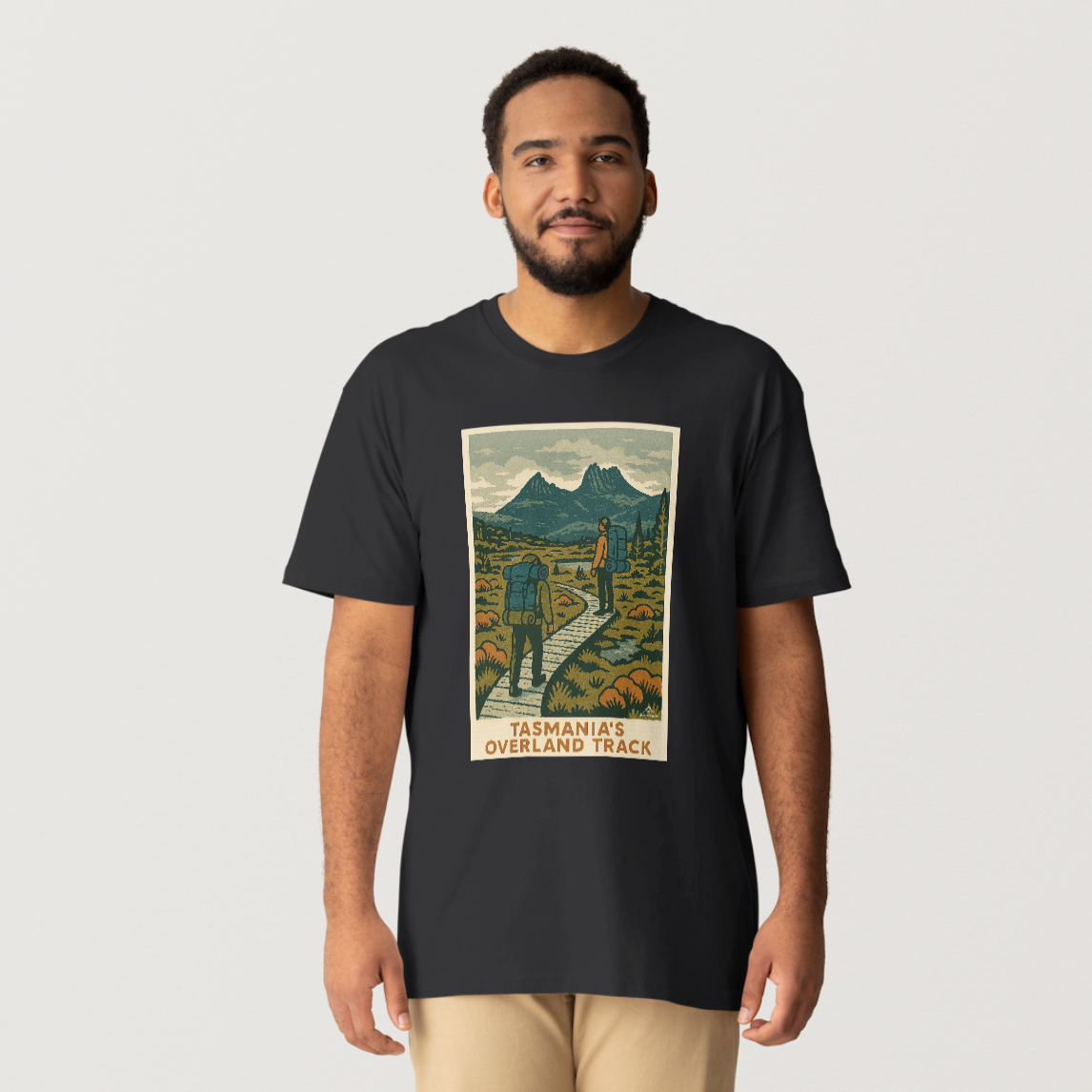 A black Overland Track Trail t-shirt featuring a graphic print of the Overland Track in Tasmania with a mountainous landscape and a hiker on the trail.